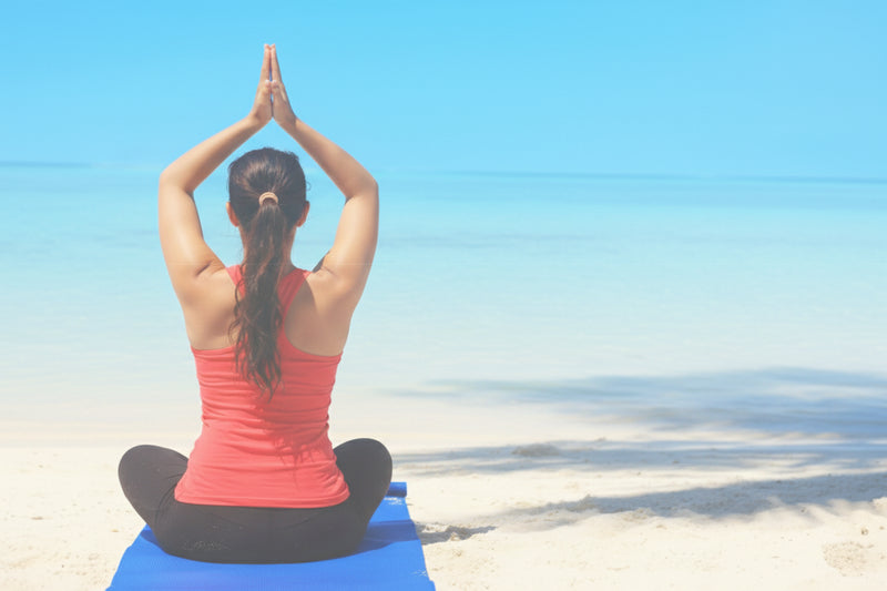 Person practicing yoga on a beach with clear blue sky